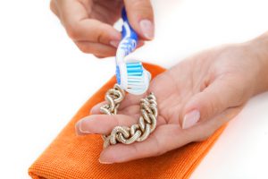 Woman's hands cleaning golden bracelet with a toothpaste
